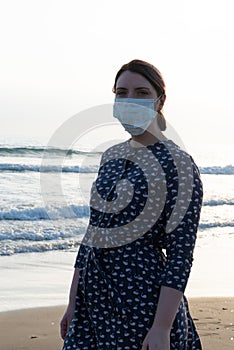 Young beautiful girl stands near the sea in a medical mask