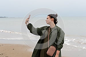 Young beautiful girl stands with a phone near the sea