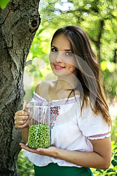 Young beautiful girl stands with a pitcher of green peas near the tree