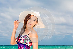 Young beautiful girl in a straw white hat on the beach of a tropical island. Summer vacation concept.