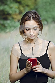 A young beautiful girl on the street uses a smartphone, listens to music on headphones