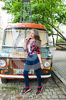 Young beautiful girl in stylish clothes in front of old broken bus posing in city street