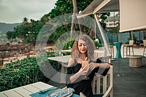 Young beautiful girl in summer bar with cocktail at sunset near the beach