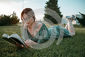 Young beautiful girl in the summer short dress reads a book sitting on the grass.