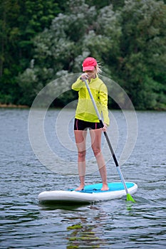 Young beautiful girl-surfer riding on the stand-up paddle board in the clear waters of the on the background of green trees