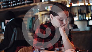 Young beautiful girl is surfing internet on phone in bar.