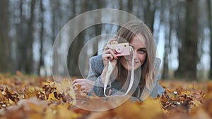 A young beautiful girl takes pictures in an autumn park using a toy camera.