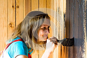 A young and beautiful girl with a tassel in her hands was very focused on painting the wooden surface in black paint.