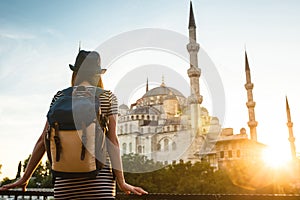 Young beautiful girl traveler in a hat with a backpack looking at a blue mosque - a famous tourist attraction of