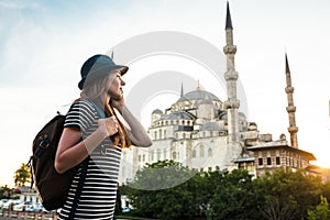 Young beautiful girl traveler in a hat with a backpack talking on a mobile phone near the blue mosque - the famous