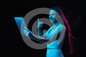 Young beautiful girl using tablet isolated on dark background in neon light