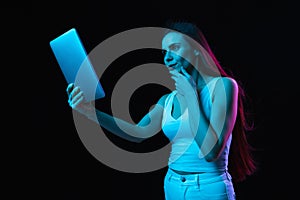 Young beautiful girl using tablet isolated on dark background in neon light