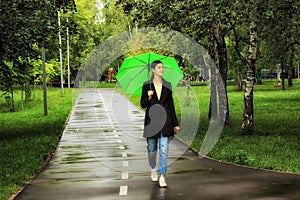 Young beautiful girl walking alone under green umbrella in the city park in summertime