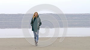 Young beautiful girl walking to camera on sandy beach and smiling in fog mist.