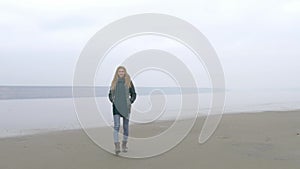 Young beautiful girl walking to camera on sandy beach and smiling in fog mist