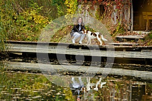 A young beautiful girl walks with a dog near a lake in an autumn park
