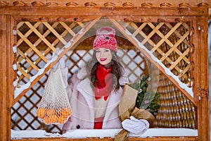 A young beautiful girl walks on a winter day in the garden in her hands holding tangerines and a bouquet of fir trees