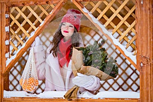 A young beautiful girl walks on a winter day in the garden in her hands holding tangerines and a bouquet of fir trees