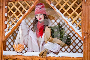 A young beautiful girl walks on a winter day in the garden in her hands holding tangerines and a bouquet of fir trees