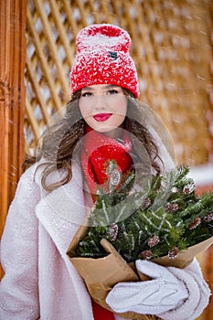 A young beautiful girl walks on a winter day in the garden in her hands holding tangerines and a bouquet of fir trees