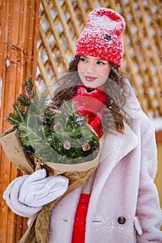 A young beautiful girl walks on a winter day in the garden in her hands holding tangerines and a bouquet of fir trees