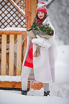 A young beautiful girl walks on a winter day in the garden in her hands holding tangerines and a bouquet of fir trees