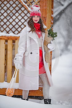 A young beautiful girl walks on a winter day in the garden in her hands holding tangerines and a bouquet of fir trees