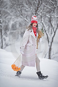A young beautiful girl walks on a winter day in the garden in her hands holding tangerines and a bouquet of fir trees