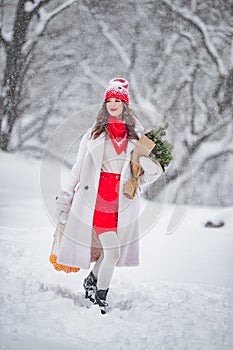 A young beautiful girl walks on a winter day in the garden in her hands holding tangerines and a bouquet of fir trees