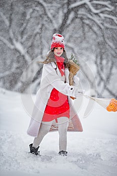 A young beautiful girl walks on a winter day in the garden in her hands holding tangerines and a bouquet of fir trees