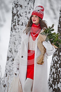 A young beautiful girl walks on a winter day in the garden in her hands holding tangerines and a bouquet of fir trees