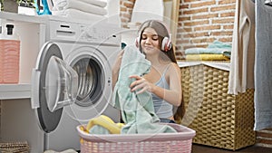 Young beautiful girl washing clothes listening to music at laundry room