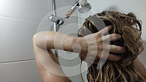 Young beautiful girl washing her hair with shampoo in the shower