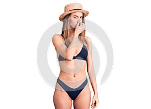 Young beautiful girl wearing bikini and hat smelling something stinky and disgusting, intolerable smell, holding breath with