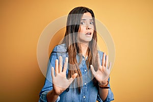 Young beautiful girl wearing casual denim shirt standing over isolated yellow background afraid and terrified with fear expression