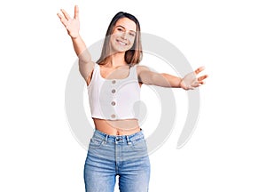 Young beautiful girl wearing casual sleeveless t shirt looking at the camera smiling with open arms for hug