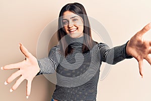 Young beautiful girl wearing casual striped t shirt looking at the camera smiling with open arms for hug