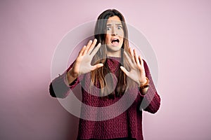 Young beautiful girl wearing casual sweater over isolated pink background afraid and terrified with fear expression stop gesture