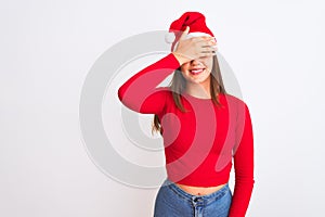 Young beautiful girl wearing Christmas Santa hat standing over isolated white background smiling and laughing with hand on face