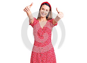 Young beautiful girl wearing dress and diadem approving doing positive gesture with hand, thumbs up smiling and happy for success