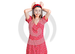 Young beautiful girl wearing dress and diadem doing bunny ears gesture with hands palms looking cynical and skeptical