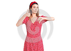 Young beautiful girl wearing dress and diadem doing thumbs up and down, disagreement and agreement expression