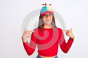 Young beautiful girl wearing fanny cap with propeller standing over isolated white background looking confident with smile on