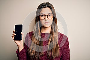 Young beautiful girl wearing glasses showing smartphone over isolated white background with a confident expression on smart face