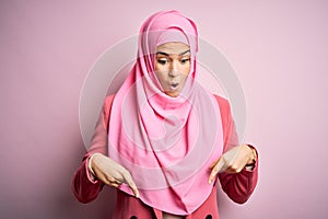 Young beautiful girl wearing muslim hijab standing over isolated pink background Pointing down with fingers showing advertisement,