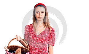 Young beautiful girl wearing picnic basket thinking attitude and sober expression looking self confident