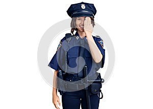 Young beautiful girl wearing police uniform covering one eye with hand, confident smile on face and surprise emotion