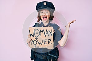 Young beautiful girl wearing police uniform holding woman power banner celebrating victory with happy smile and winner expression