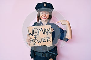 Young beautiful girl wearing police uniform holding woman power banner pointing finger to one self smiling happy and proud