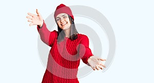 Young beautiful girl wearing sweater and wool cap looking at the camera smiling with open arms for hug